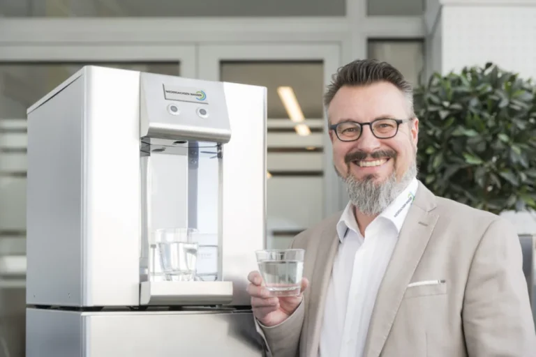 Trinkwasserspender - ein Mann hält ein frisch gezapftes Wasserglas mit Trinkwasser in der Hand